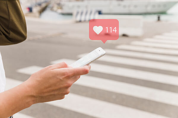 mobilni telefon u ruci na pešačkom prelazu iznad koga digitalni oblaćić predstavlja broj lajkova